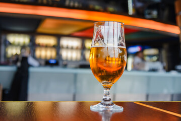 A beer in Tulip glass. Glass of light beer on wooden table in cafe or restaurant .Beautiful crystal glass with golden freshly brewed cold wheat beer stands on table cafe,restaurant terrace.