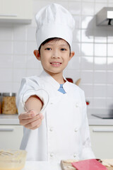 Portrait of happy smiling Asian boy in white chef uniform with hat, shows heart shaped of dough cutting, cute baker child cooking meal food at kitchen, kid chef prepares to bake bread bakery.