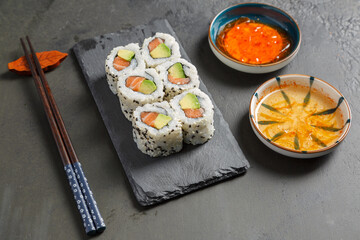 California rolls au saumon sur une ardoise avec une sauje soja et baguettes. Cusine japonaise.