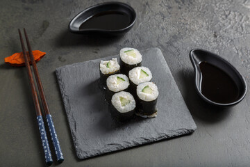 Maki au fromage et concombre - spécialité culinaire japonaise - sur une ardoise avec une sauce soja et baguettes.