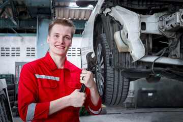 Young handsome mechanic in red uniform working with lifted vehicle, auto mechanic checking wheel at garage, technician check, repair and maintenance customer car automobile at repair service shop.