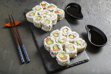 Assortiment de California rolls sur une ardoise avec une sauje soja et baguettes. Cusine japonaise.