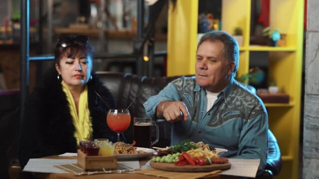 The man and woman are seated together in a restaurant, engaged in conversation. The man is attempting to get the attention of the waiter, gesturing to call him over.