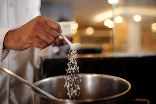 Closeup image of chef putting spoon of salt in big saucepan