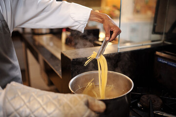 Chef using kitchen tweezers when checking if pasta is cooked