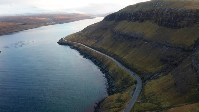 Faroe Islands 4K Aerial of Streymoy. Beautiful Sunset Aerial tracking shot following car as it drives around Streymoy with mountains on the right. Water on the left.