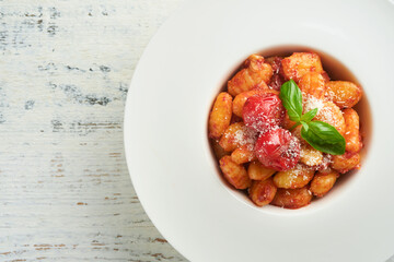 Potato gnocchi. Traditional homemade potato gnocchi with tomato sauce, basil and parmesan cheese on kitchen table on light grey kitchen table background. Traditional Italian food. Top view.