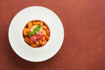 Potato gnocchi. Traditional homemade potato gnocchi with tomato sauce, basil and parmesan cheese on kitchen table on red kitchen table background. Traditional Italian food. Top view.