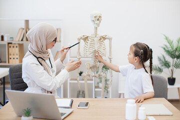 Preteen girl touching sternum on model at doctor's workplace