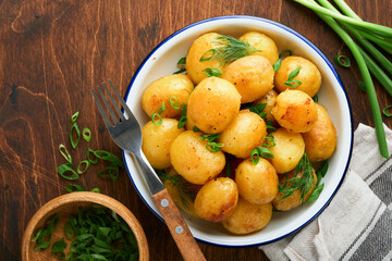 Boiled new or young potatoes with butter, fresh dill and onions in white bowl on dark old rustic wooden background. Tasty new boiled potatoes. Top view.