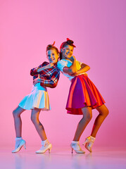 Obraz na płótnie Canvas Beautiful, stylish girls, children in retro clothes dancing lindy hop against pink studio background in neon light. Concept of childhood, hobby, active lifestyle, performance, art, fashion