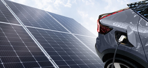 Close up of electric car with a connected charging cable on the background of solar panels.