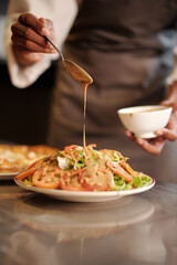 Restaurant cook pouring dressing over fresh delicious salad