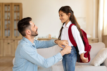Happy father preparing daughter for first school day at home