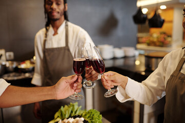 Closeup image of cooks clinking glasses of red wine after finishing work in restaurant