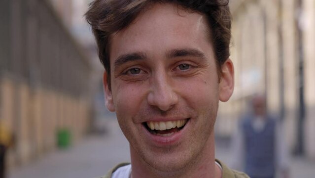 Close up face of happy young European man happy smiling on street. Male people with cheerful expression looking at camera in open air. Nice boy posing for photo outdoor. 