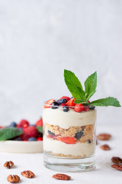 Sweet dessert in a glasses with berries, mint, nuts, whipped cream and biscuit. Vegan, sugar, gluten and lactose free.