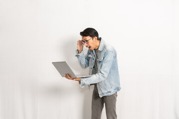 A man shock while looking at his laptop. Indonesian or southeast asian model isolated with white wall background.