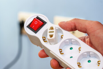 Plug adapter connected in an electrical splitter with European sockets and a red switch in hand