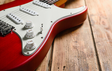 Red guitar on a wooden background. Close-up, selective focus on the tone knob. Electric guitar for...