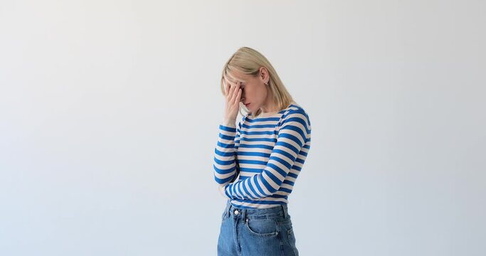 Blonde woman is seen on a clean white backdrop, expressing discomfort as she experiences a headache. She may be touching her head or rubbing her temples to convey the sensation of pain.