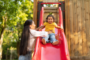 Obraz na płótnie Canvas Happy Japanese Baby Daughter Enjoying Playground Playtime With Mom Outdoors