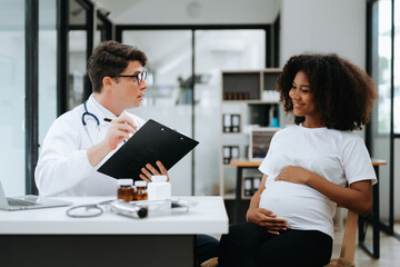 Pregnant african woman has appointment with doctor at clinic. Male gynaecologist OB GYN medic specialist with stethoscope listens to baby's heartbeat in mother's belly. Pregnancy, health care .