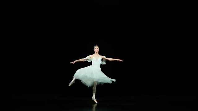 Graceful ballerina in a white dress dance and perform choreographic elements on a black background, beautiful dramatic dance with pirouettes, slow motion.