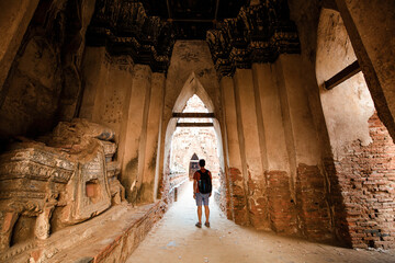 Tourist male shoulder bag walking near ancient ruined stupa with photo camera in Ayutthaya