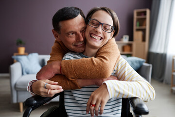 Front view portrait of caring father embracing happy girl with disability at home