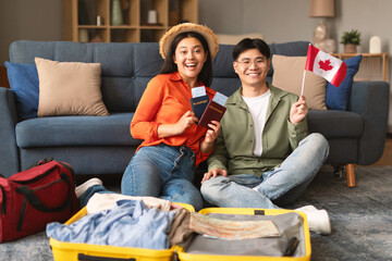 Excited Asian Couple Holding Flag Of Canada, Packing Suitcase Indoors