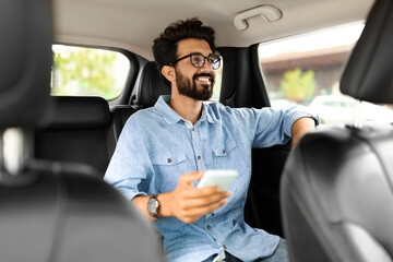 Indian man sitting on car back seat, using cell phone