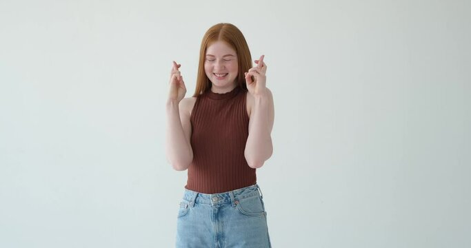 An attractive teenage girl is depicted crossing her fingers in hope on a white background. Her hopeful expression and the gesture of crossed fingers symbolize her wishful thinking.