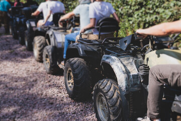Group of riders riding ATV vehicle crossing forest rural road, process of driving rental vehicle,...