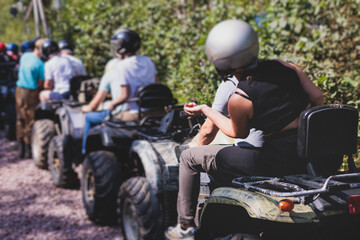 Group of riders riding ATV vehicle crossing forest rural road, process of driving rental vehicle, all terrain quad bike vehicle, during off-road tour adventure competition in a summer sunny day