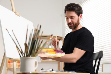 Man painting in studio. Using easel to hold canvas