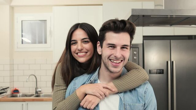 portrait of smiling young couple in the kitchen at home. Handsome man and beautiful woman standing together ans looking at camera. Lifestyle concept.