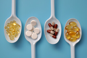 Tablets, capsules, dietary supplements, vitamins on white spoons. Medical background with pills - obrazy, fototapety, plakaty