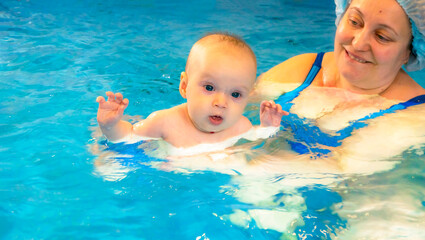 Fototapeta na wymiar Adorable baby girl enjoying swimming in a pool with her mother early development class for infants teaching children to swim and dive. Swimming instructor doing exercises with a small child in the