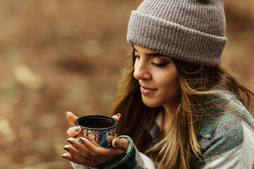 Cheerful young caucasian lady in jacket in forest drinks cup of tea, enjoy travel, vacation and hot coffee