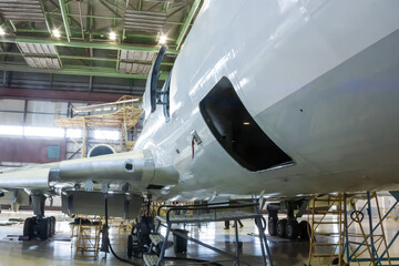 White passenger aircraft in the hangar. Airplane under maintenance. Checking mechanical systems for flight operations