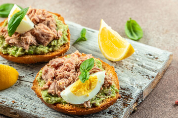 Avocado, canned tuna and boiled egg toast on a wooden board. Restaurant menu, dieting, cookbook recipe top view - obrazy, fototapety, plakaty