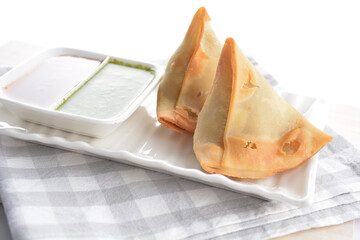 deep fried indian curry potato vegetable samosa snack with green mint yogurt sauce on white...