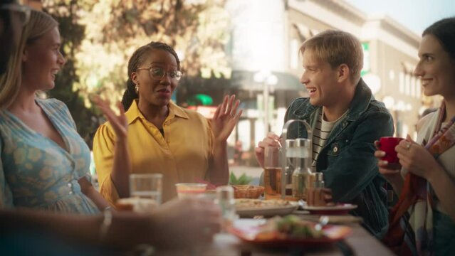 Young African Female Telling Funny Life Stories While Sitting on a Terrace with Multiethnic Friends. Young Men and Women Gathered Together in a Cafe, Spending a Beautiful Weekend Together