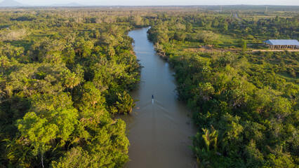 Aerial view of an engine boat passing through a river with brown river water against the sky and trees in the background - Powered by Adobe