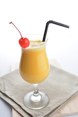 cold iced summer orange mango fruit juice with red cherry in cocktail glass black straw on grey cloth white background asian beverage halal food drink menu for hotel bar cafe