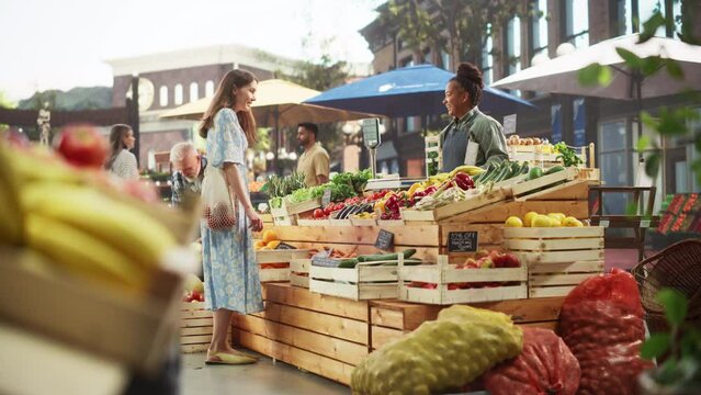 Middle Aged Diverse Couple Running a Small Business on a Farmers Market, Selling Organic Fruits and Vegetables. Young Female Shopping For Food, Choosing a Fresh Courgette or Zucchini