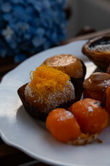 Mix of traditional Portuguese egg yolk sweets from Porto region on white plate with blue hydrangea on background.