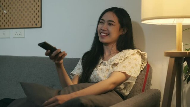 Slow motion shot of smiling young woman wearing casual clothes, relaxing on the couch watching TV