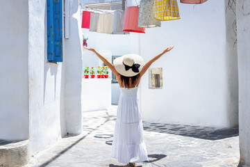 A happy tourist woman in a white summer dress walks through the whitewashed streets of Naxos island, Cyclades, Greece